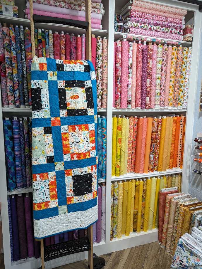 Art Gallery Quilt featured on a ladder with bolts of fabric in the background